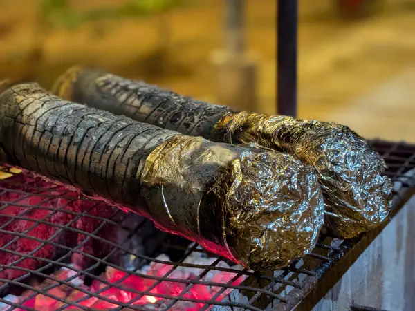 Bamboo chicken wrapped in leaves roasting over coals